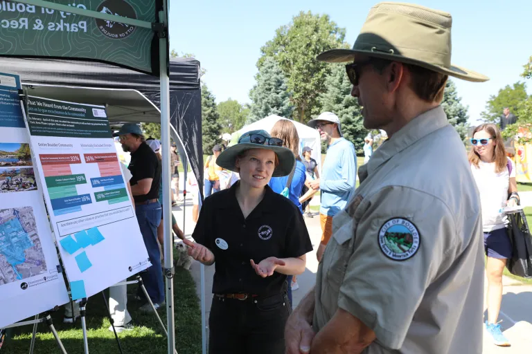 Boulder Parks and Rec employee and OSMP employee speaking together in front of a display at What's Up Boulder event