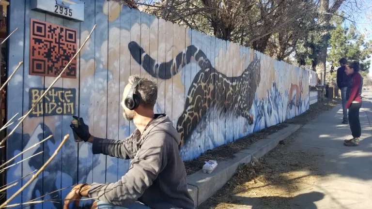 Artist painting a cheetah on the side of a fence