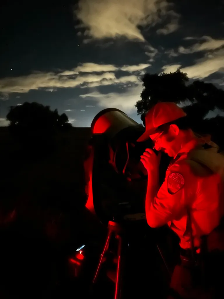 Ranger looking through the lens of a telescope on a dark night