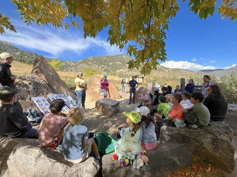 Group of young people sitting outside on rocks listening to adults speak