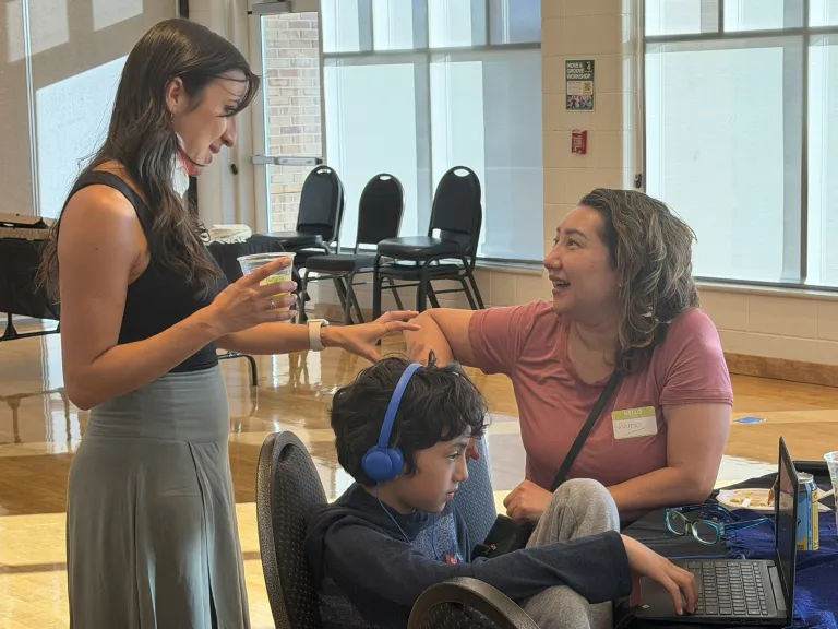 Right profile of city staff member, standing talking with community member sitting at table with son