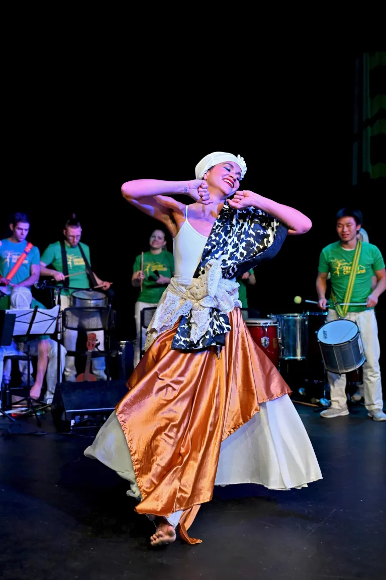 Afro-Brazilian dancer on stage with musicians in the background.