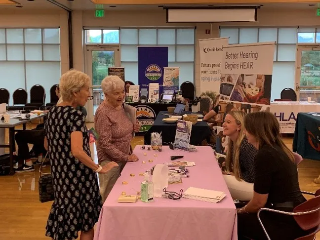 Two older adult women speaking with outreach staff during an assistive technology fair. 
