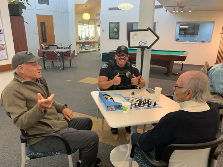 Two older adult men playing a game with a Boulder Police Officer who is giving two thumbs up to the camera.