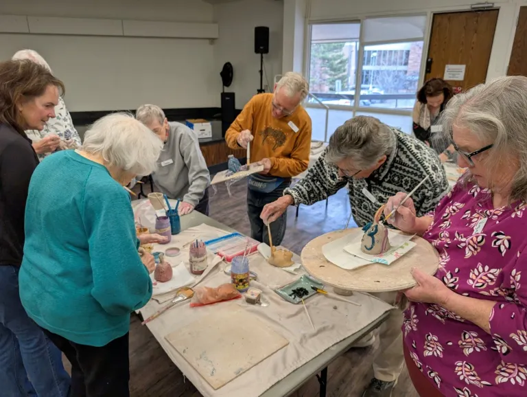 Group of older adults around a table working on pottery pieces during a pottery class. 