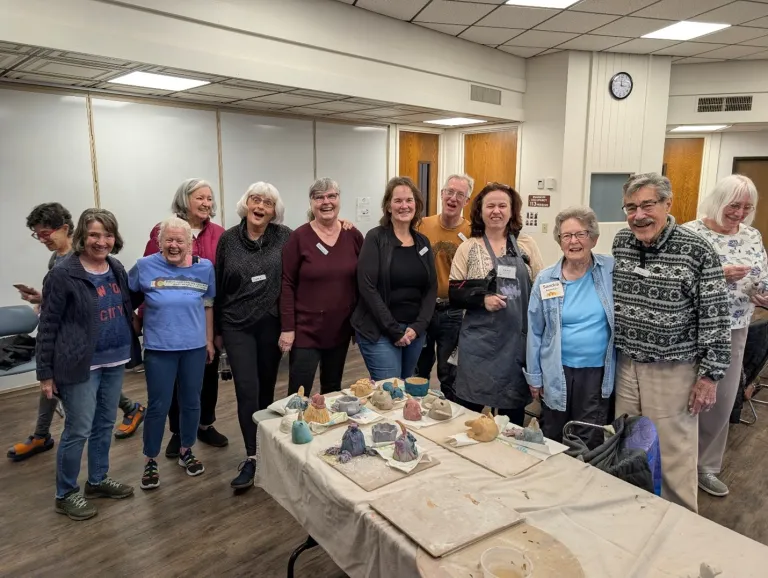 Group of older adults posing behind a table displaying their finished pottery pieces. 