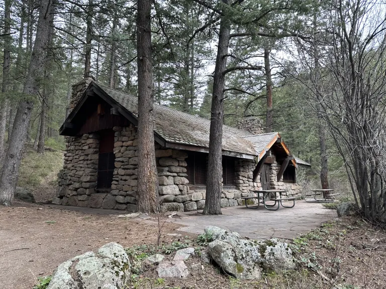 Green Mountain Lodge, stone building surrounded by pine trees with a stone patio and picnic tables.