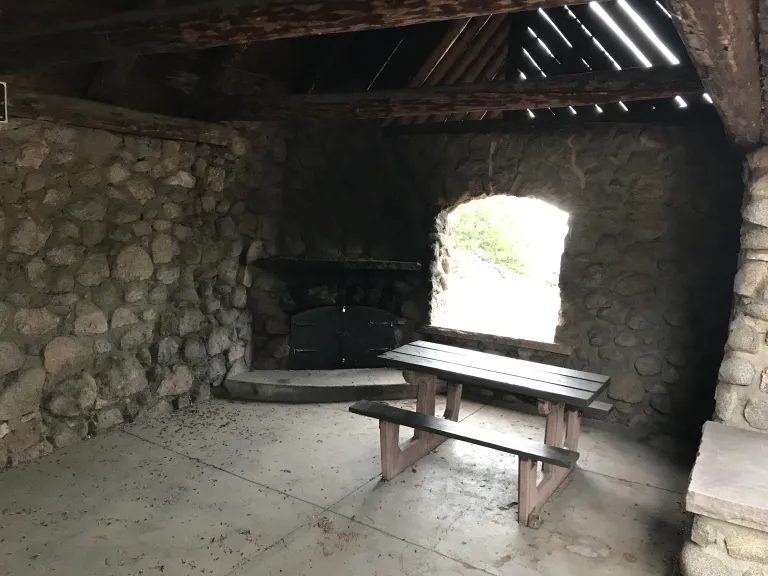 Inside the Stone Shelter, the east side has a picnic table and non-operational fireplace in the corner.