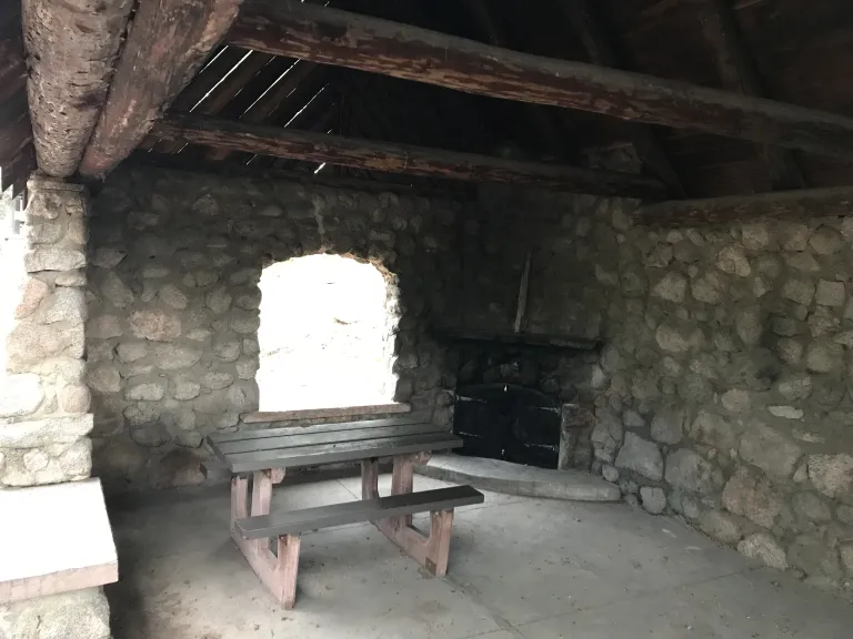 Inside the Stone Shelter, the west side has a picnic table and non-operational fireplace in the corner.