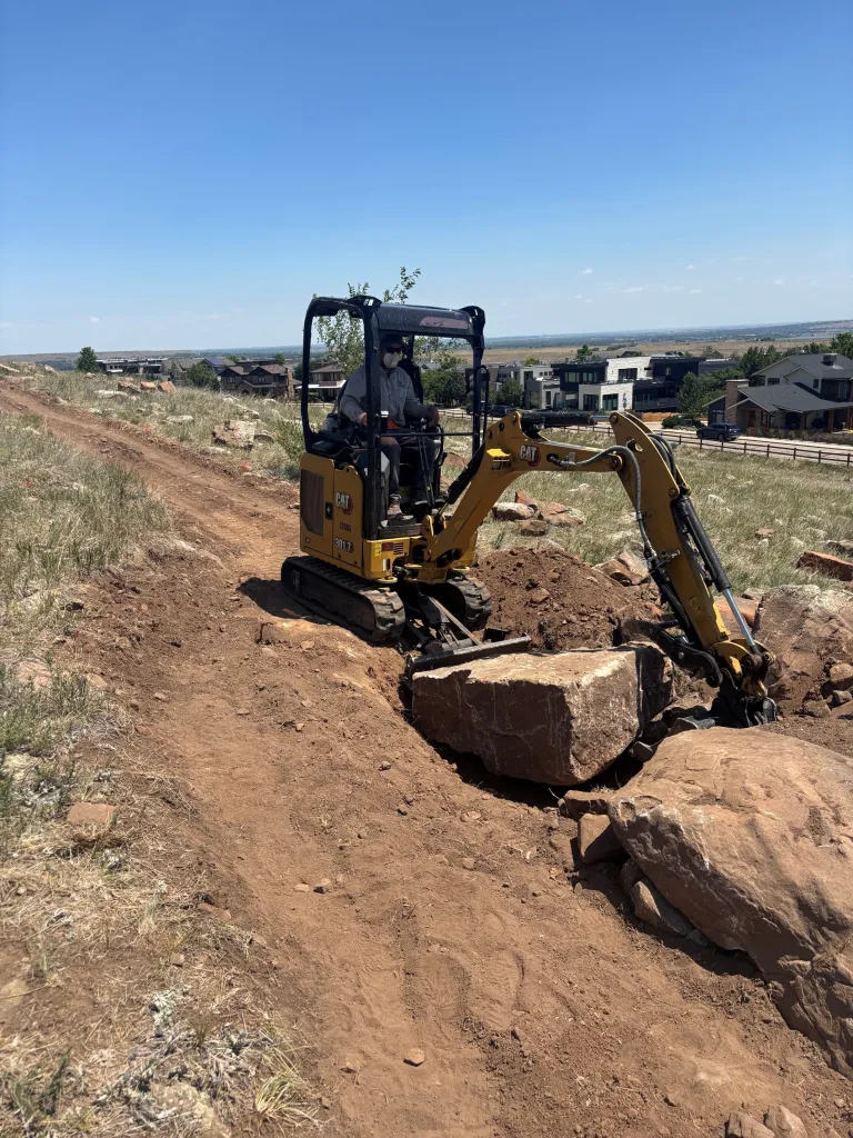 A person sits in a small construction equipment vehicle moving a large rock.