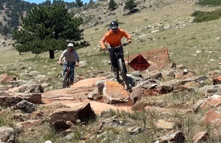 Two mountain bikers riding over a large rocks on the North Foothills Trail