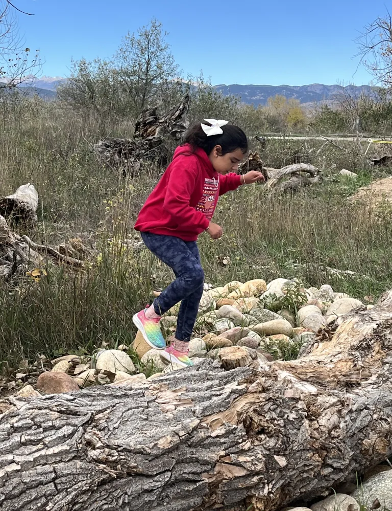 A young girl in the red jacket balances on a fallen log at Sawhill Ponds.