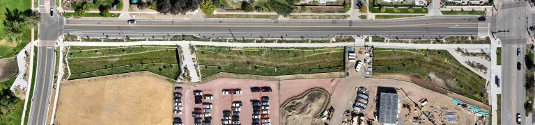 Aerial view straight down on the long, terraced flood channel running between the roadway and a construction site with a gravel parking lot.