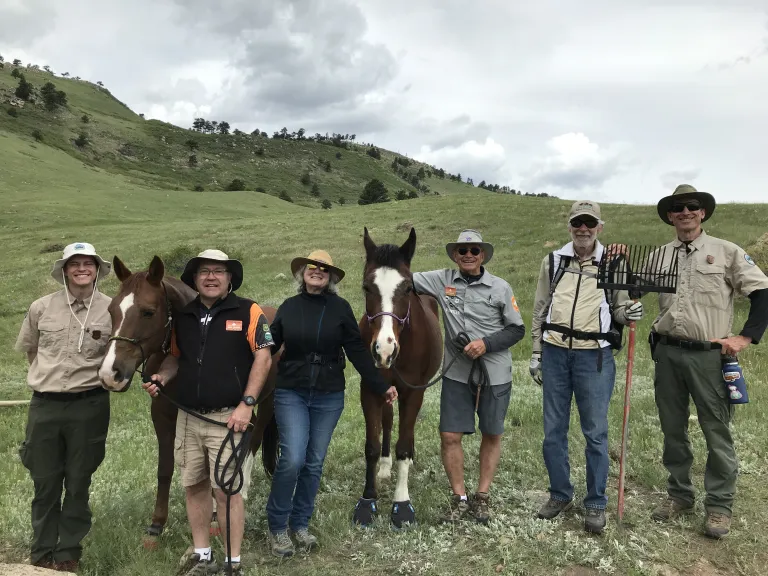 A group of people standing at the base of a green mountain two horses.