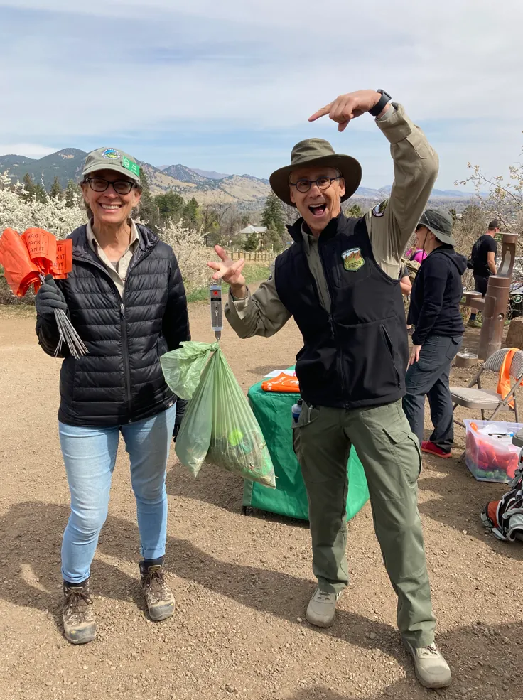 Someone enthusiastically pointing at another person holding a bunch of poop bags and orange flags.