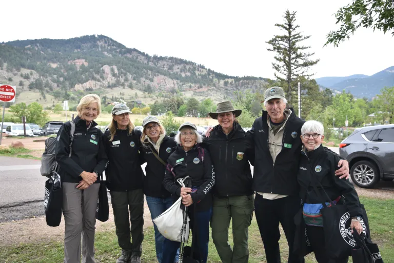A group of people in black volunteer jackets against the Flatiron Mountains.