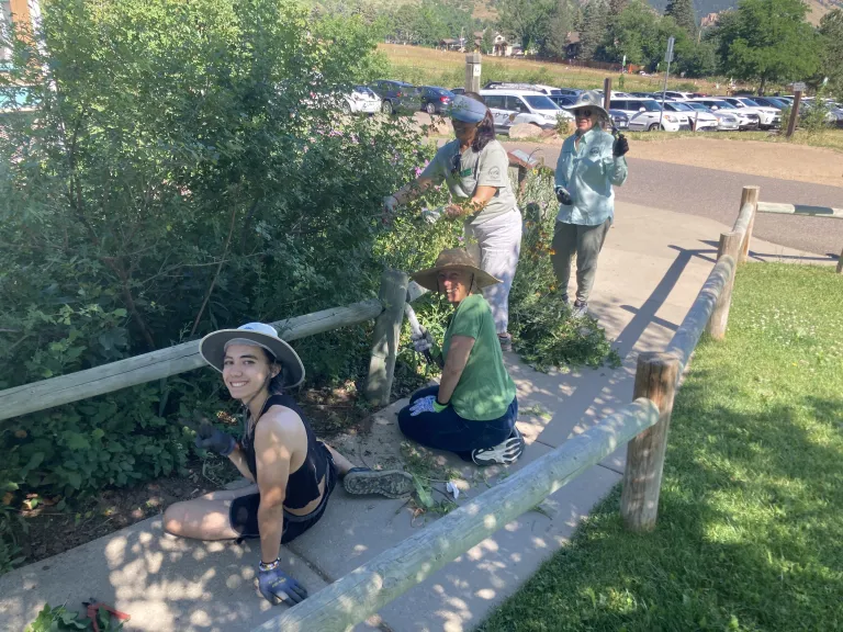 People sitting on a sidewalk next to a garden smiling at the camera.