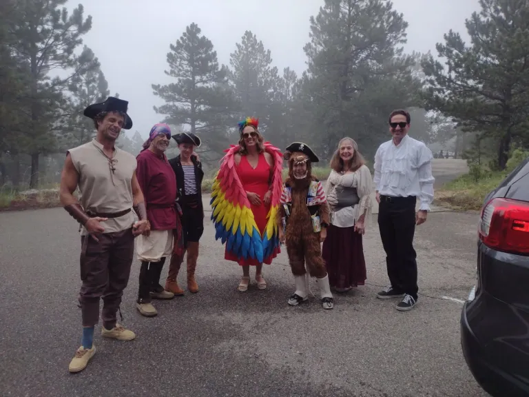 A group of people standing in a parking lot wearing pirate and parrot costumes.