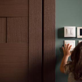 A brown-haired young girl fiddles with the thermostat in her home