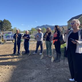 five individuals with shovels ready to break ground, one speaker presenting in the foreground