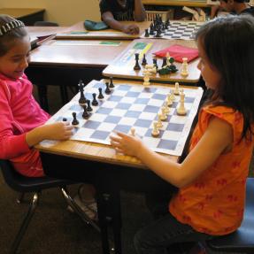 Two young girls playing chess on a school desk