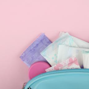 Various menstrual products, including pads and tampons, sticking out of a teal blue bag