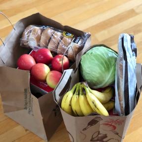 Two paper bags full of groceries. Groceries include apples, bagels, bananas and cabbage.
