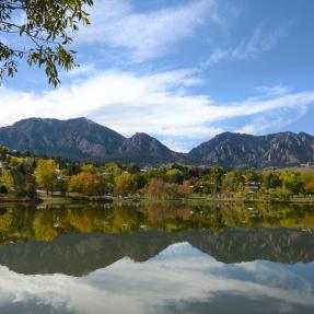 Distant view of the Flatirons with trees and water in closer view