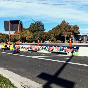 People installing murals by artist Talia Swartz Parsell on tall concrete curbs at Baseline Road