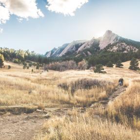Boulder Flatirons with a trail surrounded by brown grass in the foreground. 