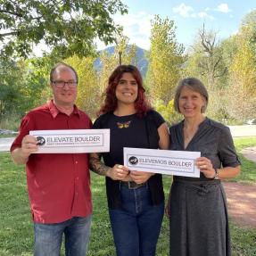 Three people holding Elevate Boulder signs