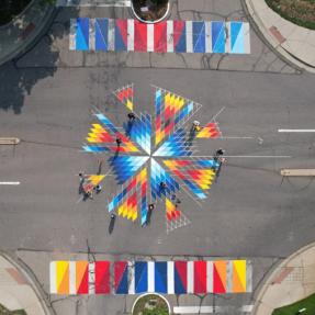 An aerial shot of a colorful and geometric mural on the pavement in the middle of a Boulder intersection
