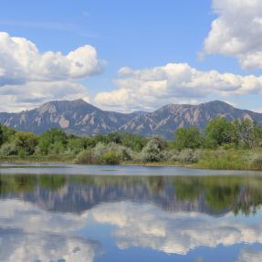 Sawhill Ponds in spring reflecting bright green trees, flatirons and white clouds in the water