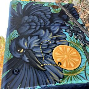 Mural of a bird holding an object on the side of an electrical box