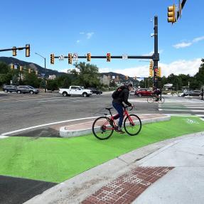 Person biking next to corner island on protected bike lane at intersection