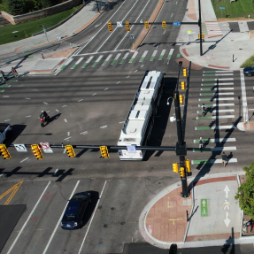 People traveling on the 28th Street and Colorado Avenue protected intersection. There are people biking, walking, taking the bus and driving.