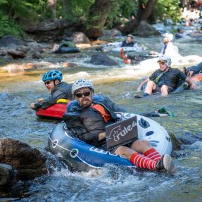 Person wearing a suit and holding a fake laptop tubing down the Boulder Creek