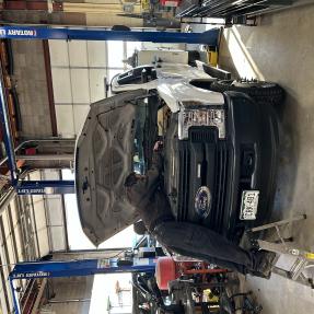 A City of Boulder mechanic working beneath the open hood of a pickup truck in the fleet garage.