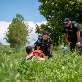 A male and female police officers bending over to talk with a woman and a child wearing a bicycle helmet on one of Boulder’s creek paths.