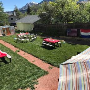 Backyard set up for a party with flags, set picnic tables and folding chairs places in a cirlce. 