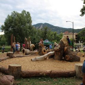 Nature play area climbing feature with children and flatirons in the background
