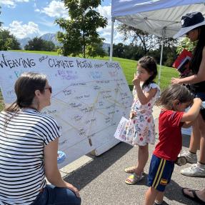 woman kneeling next to a sign with yard markers talking to kids