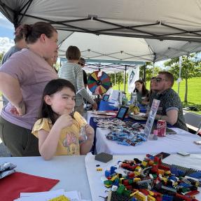 Young girl eating a popsicle and smiling while standing next to family in front of table