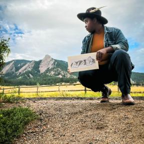 Artist poses with a sketch of the Flatirons at the base of Chautauqua. 