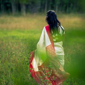 Woman walking away from the camera into a grassy field. The shot is artistically obscured by blurry leaves. 
