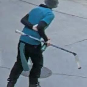 Back facing image of man in blue shirt, long sleeves, helmet and skates holding a hockey stick