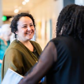 Ingrid Castro-Campos speaking with Alexis Miles from Motus Theater in the Dairy Arts Center lobby. 