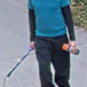 Front facing image of man in blue shirt, long sleeves, helmet and skates holding a hockey stick