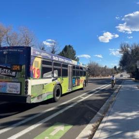 bus driving on road next to person biking besides buffered bike lane and sidewalk
