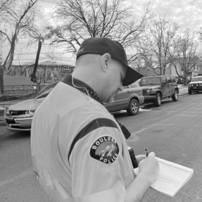 BPD Officer completes paperwork while standing on the side of a street with cars